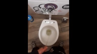 Young man pissing in a bar toilette